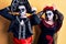 Young couple wearing mexican day of the dead costume over yellow doing bunny ears gesture with hands palms looking cynical and