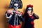 Young couple wearing mexican day of the dead costume over yellow punching fist to fight, aggressive and angry attack, threat and