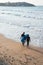 Young couple with wetsuits and surfboards enter the water to surf at San Lorenzo beach, Gijon, Spain. Seen from their back