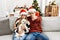 Young couple of wife and husband sitting on the sofa wearing christmas hat at home pointing with finger to the camera and to you,