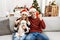 Young couple of wife and husband sitting on the sofa wearing christmas hat at home screaming proud, celebrating victory and