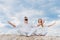 young couple on yogi meditating while sitting on sandy dune in lotus pose