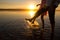 Young couples is walking in the water on summer beach. Sunset over the sea.Two silhouettes against the sun. Feet doing splashes of