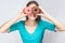 Young crazy girl bite one lips in blue blouse standing, holding, covering eyes with pink and chocolate donuts,looking through don