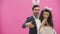 Young creative couple on pink background. With hackneyed ears on the head. During this time, they show the gestures of