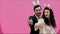 Young creative couple on pink background. With hackneyed ears on the head. During this time, they show the gestures of