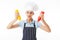 Young cunning woman chef in striped apron and white hat dreamily looking aside while holding bottles of ketchup and