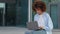 Young curly african american girl woman with afro hairstyle sitting outdoors on street in city in business part near