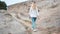 Young curly blonde woman in jeans and a white shirt walks on the background of the ancient city. Tourist in picturesque