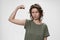 Young curly hair woman shows muscle on her hand, feels proud to be strong