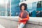 Young curly mixed-race boy drinks coffee on the street against the background of office buildings.