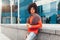 Young curly mixed-race boy drinks coffee on the street against the background of office buildings. Youth culture and fashion.