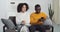 Young curly wife afro american girl and mixed race black husband guy with glasses sitting together on blanket on sofa in