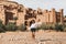 Young curly woman walking on background of Ait-Ben-Haddou. Travel in Morocco