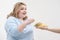 Young curvy fat woman in casual blue clothes on a white background sneaking off a plate of hamburger and french fries