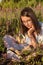 A young cute attentive girl lies on the green grass and reads a book illuminated by the setting sun.