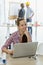 Young cute and beautiful secretary in company sitting beside white hard safety hat and using labtop notebook computer to work with