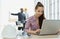 Young cute and beautiful secretary in company sitting beside white hard safety hat and using labtop notebook computer to work with