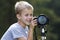 Young cute blond child boy taking picture with tripod camera on