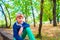 A young and cute boy in green jeans sits on a curb in a park with his hand on his knee