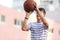 A young cute boy plays basketball at the outdoor streetball court on a sunny summer day. Teenager player in action with the ball.