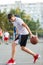A young cute boy plays basketball at the outdoor streetball court on a sunny summer day. Teenager player in action dribbling