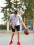 A young cute boy plays basketball at the outdoor streetball court on a sunny summer day. Teenager player in action dribbling