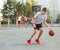 A young cute boy plays basketball at the outdoor streetball court on a sunny summer day. Teenager player in action dribbling