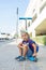 Young cute boy is sitting on the Kick scooter at a bus stop near the Emirates Mall in Dubai, waiting for the bus. United Arab Emir