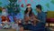 Young cute couple exchanging festival gifts while sitting under a decorated Christmas tree