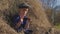 Young cute girl with a cap having fun, sits in a haystack and use phone. Little girl sitting on hay.