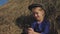 Young cute girl with a cap having fun, sits in a haystack and use phone. Little girl sitting on hay.