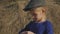 Young cute girl with a cap having fun, sits in a haystack and use phone. Little girl sitting on hay.