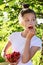 young cute girl in white T-shirt holds a glass vase with ripe cherries and brings one berry to her mouth.