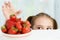 Young cute smiling european little girl is trying to steal ripe jucy strawberry from plate of many berries while she