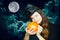 A young cute witch on Halloween with a pumpkin on the background of a creepy dark magical sky. A girl in a witch`s hat hugs a pump