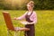 Young cute woman artist finishes painting with pleasant facial expression, posing isolated on meadow background, stands in front