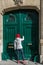 Young cute woman with red hat and shoes, knocking at a vintage green wooden door.