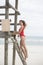 Young cute woman in red monokini on a wooden lifeguard tower