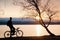 Young cyclist silhouette on blue sky and sunset background on beach. End of season at lake.