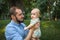 Young dad holding baby son on the background of a summer landscape. Father looks at his child, the newborn with a confused face