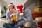 Young dad kissing hand of a baby in mothers arms, laughing, wearing santa hats