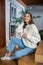 Young dark-haired pretty woman in jeans and white sweater sitting on stairs