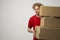 Young delivery man in a red uniform holding a stack of cardboard boxes. Courier delivering postal packages, parcels over