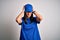 Young delivery woman with blue eyes wearing cap standing over blue background suffering from headache desperate and stressed