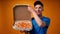 Young deliveryman in blue uniform opens a box of fresh pizza against yellow background