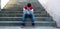 Young depressed caucasian man, with his hands on his face,sitting on some stairs outdoors, with a face mask