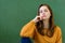 Young depressed female high school student sitting in front of chalkboard in classroom, with her hand on chin.