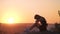 Young depressed woman in black short summer dress sitting on a mountain hill thinking outdoors at sunset. Lonely female contemplat