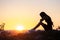 Young depressed woman in black short summer dress sitting on a rock thinking outdoors at sunset. Fashionable female contemplating